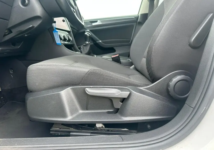 Vue intérieure côté conducteur de la Volkswagen Golf blanche 2018, mettant en valeur le siège avant gris et la console centrale.