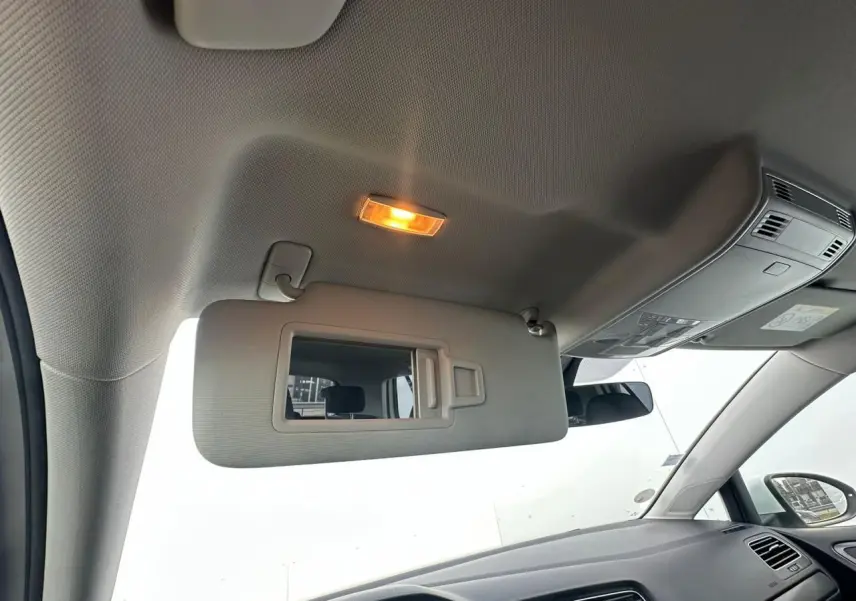 Vue intérieure côté conducteur de la Volkswagen Golf blanche, montrant le pare-soleil avec miroir éclairé et tableau de bord.