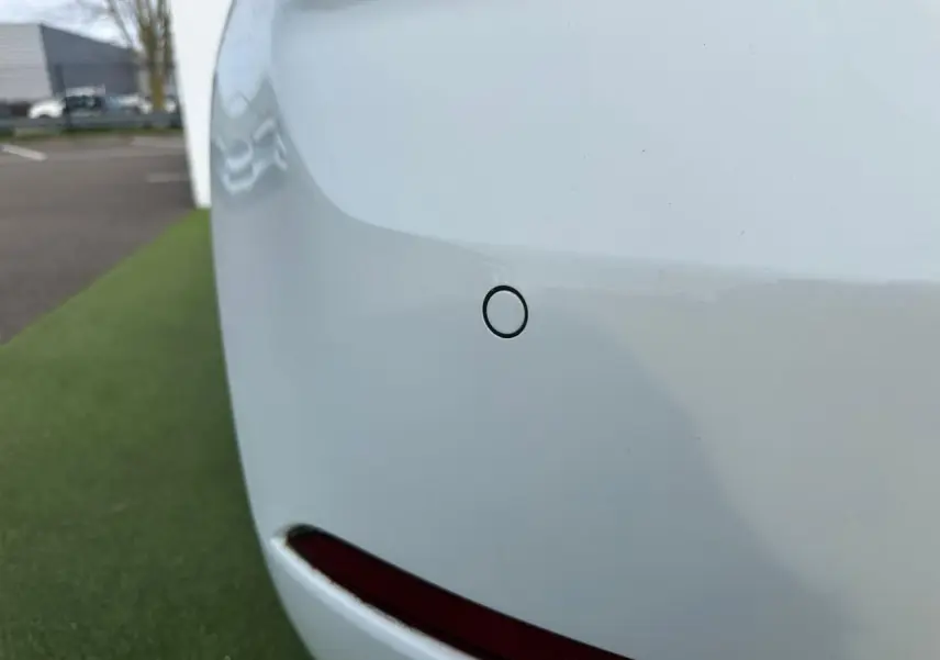 Gros plan sur le pare-chocs arrière blanc d'une Volkswagen Golf VII avec capteur de stationnement visible.