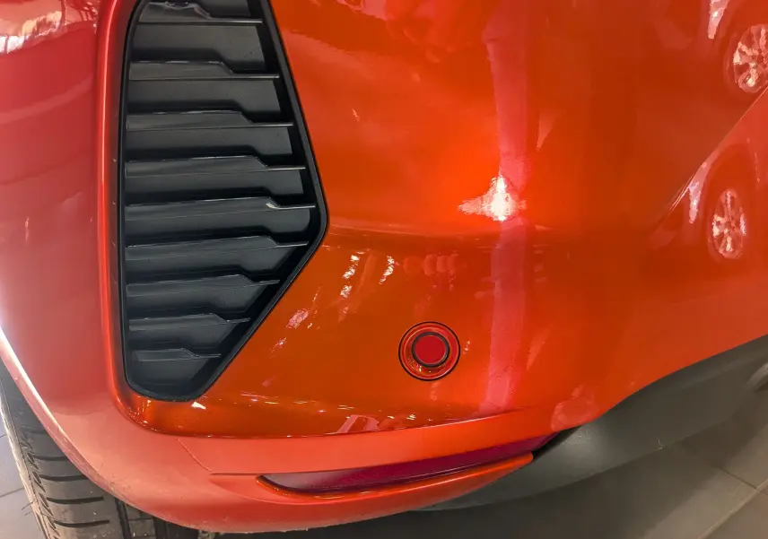 Gros plan sur le pare-chocs arrière orange Valencia de la Renault Clio V avec capteur de recul et diffuseur noir.