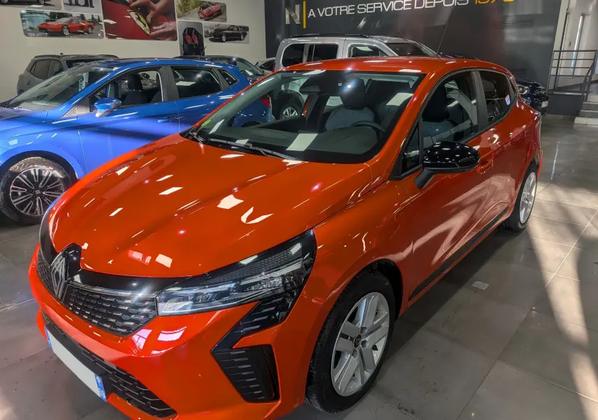 Renault Clio V Orange Valencia vue 3/4 avant droit en showroom, avec calandre noire et phares LED distinctifs.