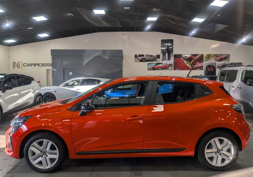 Renault Clio V Blue dCi 100 en Orange Valencia vue de profil côté gauche dans un showroom lumineux.