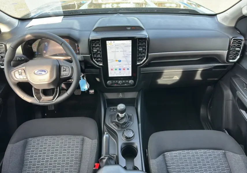 Vue intérieure avant du Ford Ranger 2026, tableau de bord noir avec écran tactile vertical et volant cuir multifonctions.