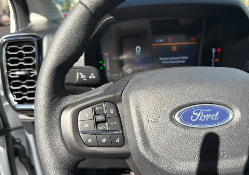Gros plan sur le volant cuir multifonctions du Ford Ranger blanc glacier, avec tableau de bord numérique en arrière-plan flou.