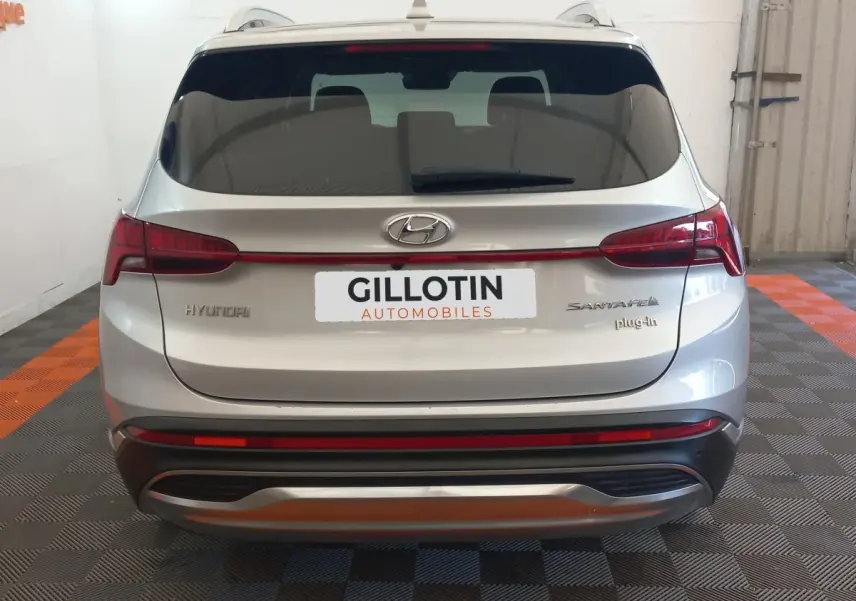 Vue arrière d'un Hyundai Santa Fe gris clair hybride rechargeable avec logo et badges visibles, dans un garage.