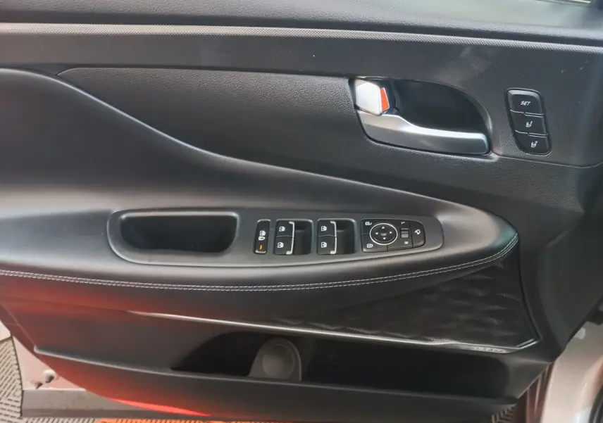 Gros plan sur la porte avant gauche intérieure du Hyundai Santa Fe gris clair, avec commandes de vitres et réglages mémoire.