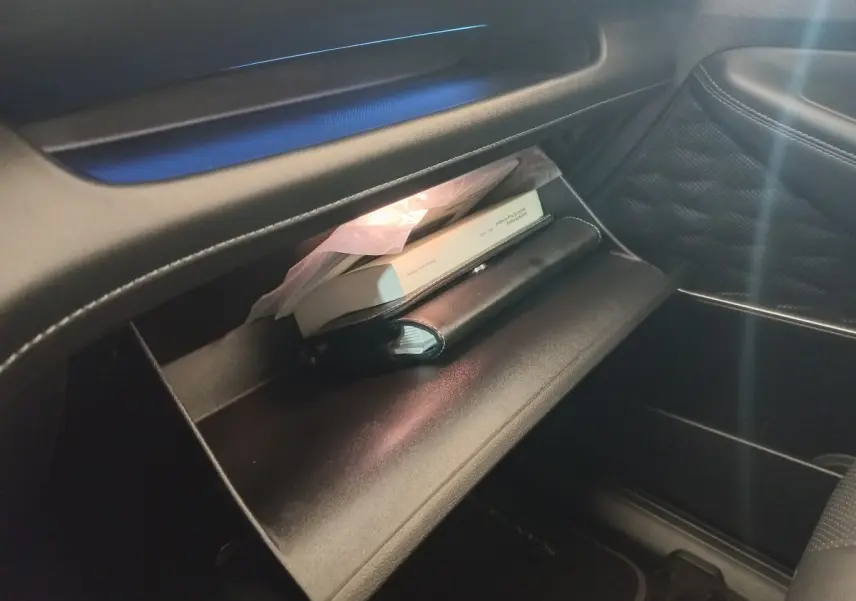 Intérieur du Hyundai Santa Fe hybride 2021, vue sur la boîte à gants ouverte avec documents et éclairage intérieur.