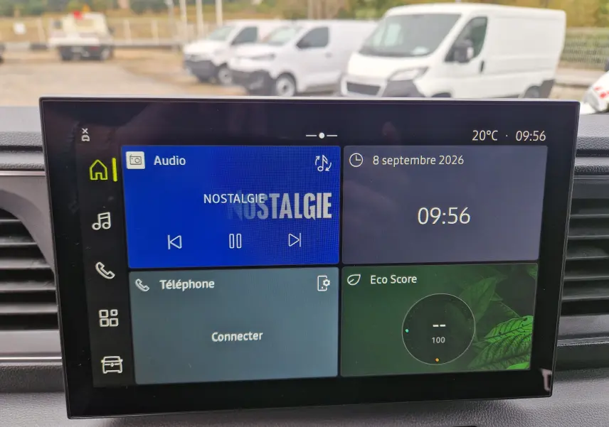 Vue intérieure centrée sur l’écran multimédia openR Link 10'' du Renault Master gris urbain, avec vue floue de fourgons blancs à l’arrière.