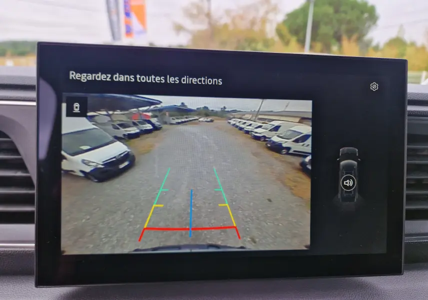 Vue écran caméra de recul du Renault Master gris urbain, montrant une allée avec plusieurs véhicules blancs stationnés de chaque côté.
