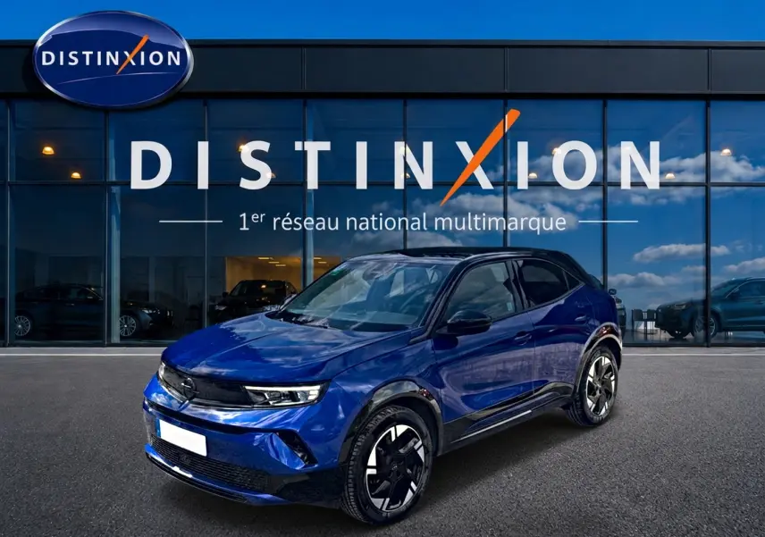 Opel Mokka Electric bleu en 3/4 avant droit, avec jantes alu noires et toit noir devant showroom Distinxion.