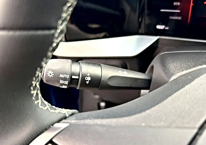 Gros plan sur la commande des feux et clignotants à gauche du volant dans l’habitacle noir de l’Opel Mokka Electric 2025.