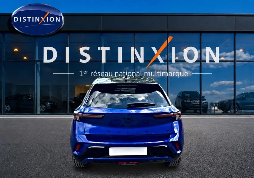 Vue arrière d'un Opel Mokka Electric 156 GS bleu garé devant une vitrine avec logo Distinxion.