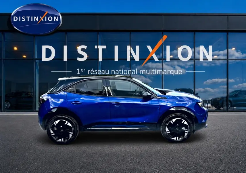 Opel Mokka Electric bleu en profil droit, avec jantes alu noires et toit noir devant une vitrine Distinxion.