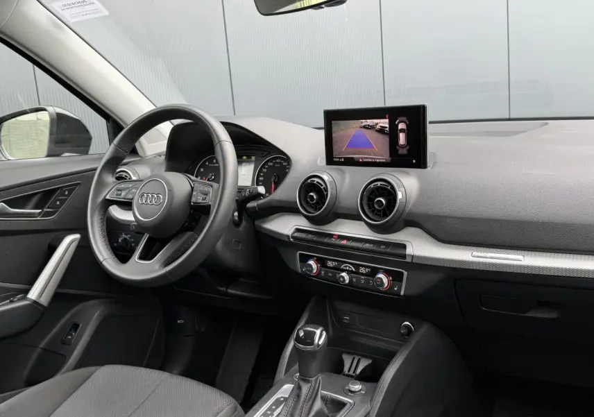Intérieur Audi Q2 35 TFSI 2023 vu côté conducteur, tableau de bord noir avec écran caméra de recul et climatisation.