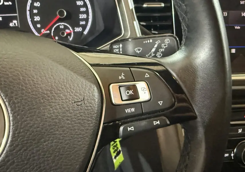 Gros plan sur le volant cuir noir du Volkswagen T-Roc 2020 avec commandes multifonctions et tableau de bord partiellement visible.