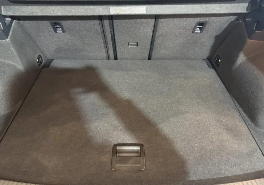 Coffre spacieux et propre du Volkswagen T-Roc noir, vue plongeante montrant le tapis de sol et les fixations arrière.