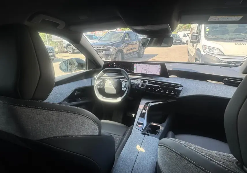 Vue intérieure avant du Peugeot 3008 Hybrid 136 e-DCS6 Allure 2025, mettant en valeur le cockpit numérique et les finitions tissu gris.