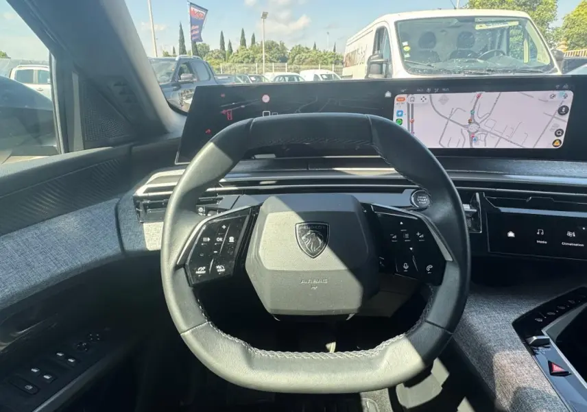 Vue intérieure centrée sur le volant compact et le cockpit numérique du Peugeot 3008 Hybrid gris foncé, avec écran tactile visible.