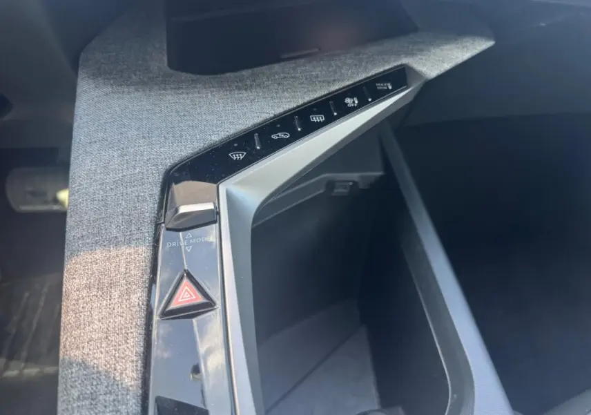 Vue rapprochée de la console centrale grise du Peugeot 3008 Hybrid 2025 avec boutons de contrôle et rangement ouvert.