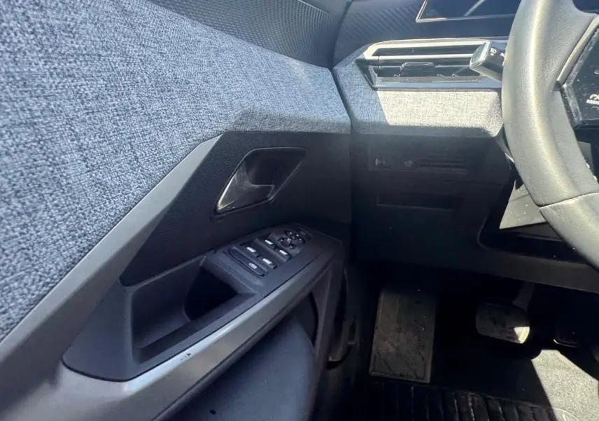 Vue intérieure côté gauche du Peugeot 3008 Hybrid 136 e-DCS6 Allure 2025, montrant la porte avec commandes électriques et tissu gris.