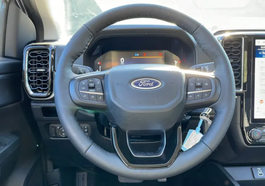 Vue intérieure centrée sur le volant cuir multifonctions du Ford Ranger gris avec tableau de bord digital et écran tactile.