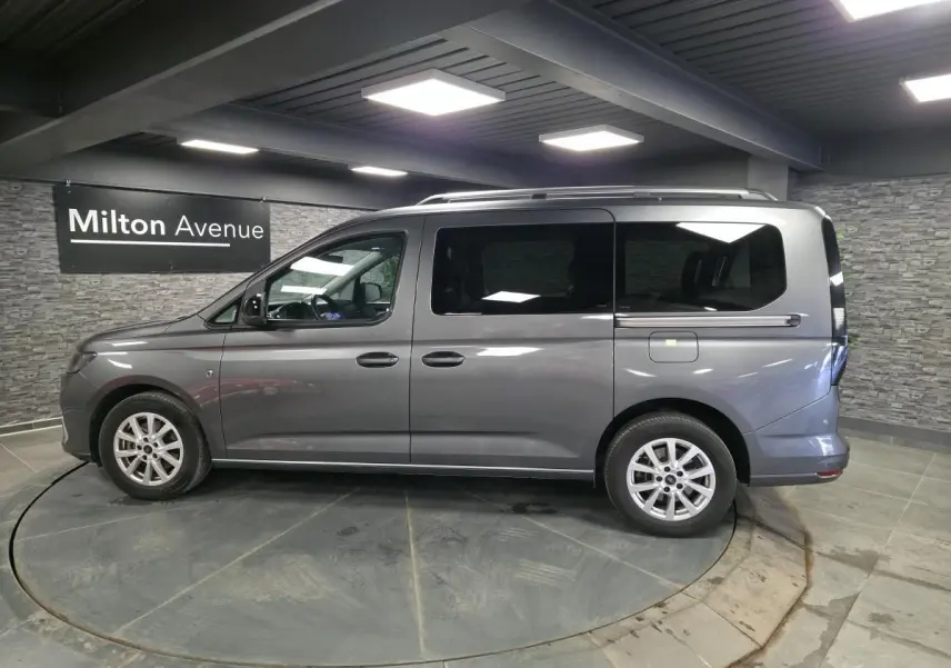 Vue de profil côté gauche d'un Ford Transit Connect gris 2023 avec portes coulissantes et barres de toit argentées.