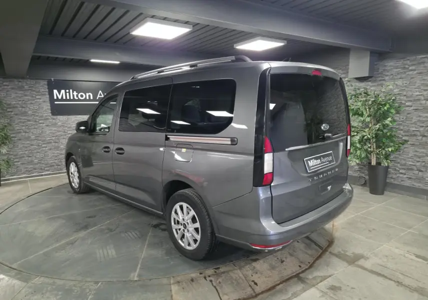 Vue 3/4 arrière droite du Ford Transit Connect gris avec barres de toit argentées et vitres arrière surteintées.