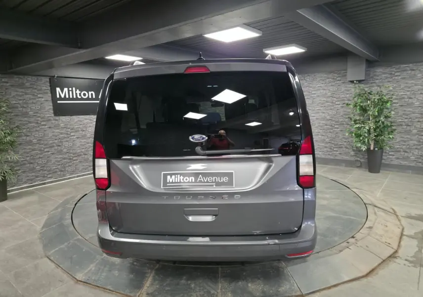 Vue arrière d'un Ford Tourneo Connect gris 2023 avec hayon vitré et feux arrière verticaux dans un showroom.