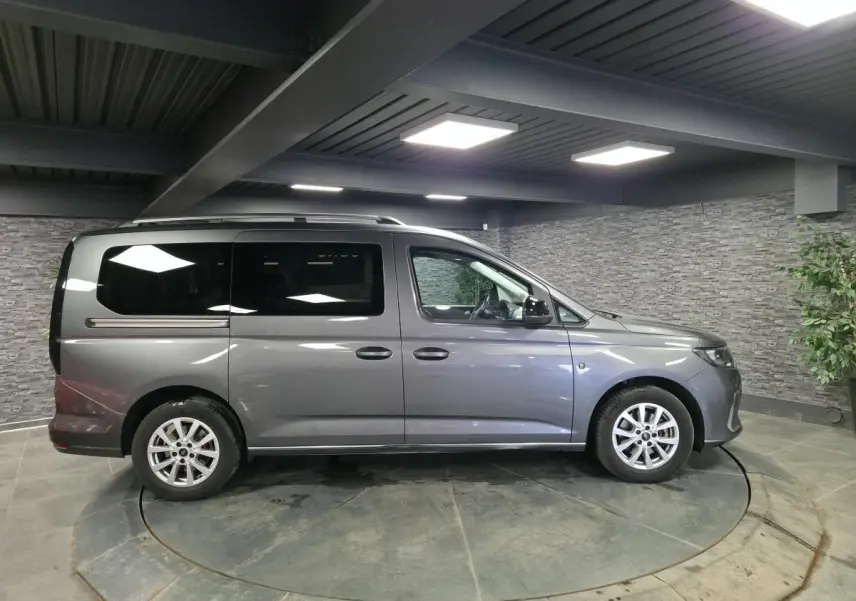 Vue latérale droite d'un Ford Transit Connect gris métallisé avec barres de toit argentées dans un showroom.