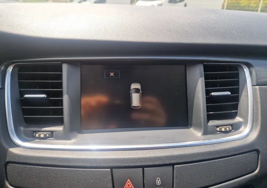 Vue rapprochée de l’écran central du tableau de bord de la Peugeot 508 SW 2015, entouré de grilles d’aération noires.