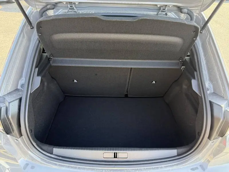 Coffre ouvert vu de dessus d’une Peugeot 208 gris Selenium, montrant un espace de rangement propre et vide.