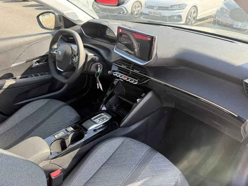 Vue intérieure avant droite de la Peugeot 208 1.2 Hybrid 110ch Allure avec tableau de bord noir et sièges tissu gris.
