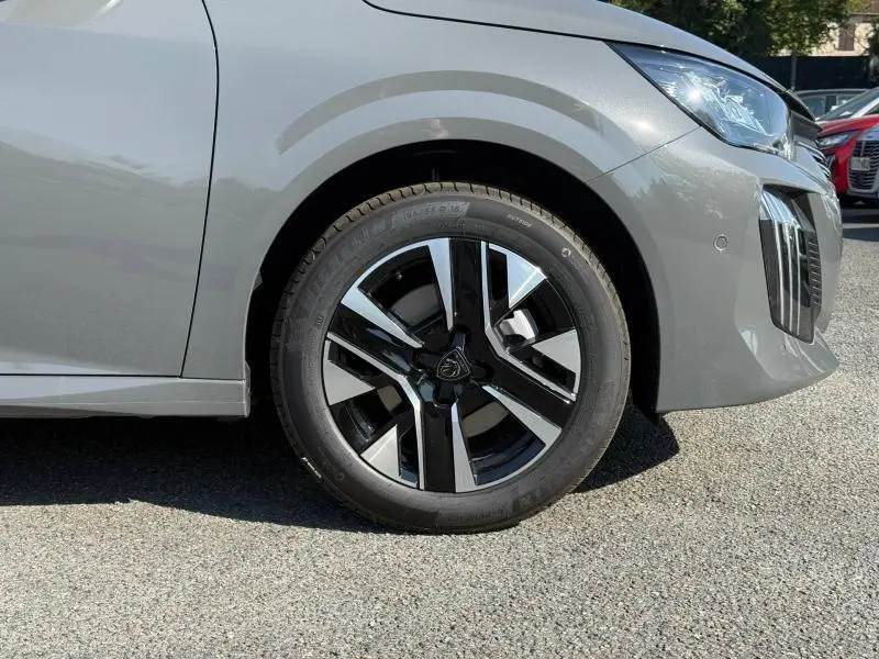Gros plan sur la roue avant droite et l'aile d'une Peugeot 208 gris Selenium avec jante alu bicolore moderne.