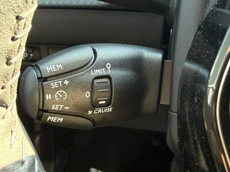 Gros plan sur la commande de régulateur de vitesse du Peugeot 208 1.2 Hybrid 110ch Allure gris Selenium, côté gauche du volant.
