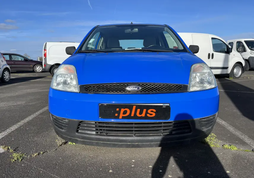 Vue frontale d'une Ford Fiesta bleue 3 portes de 2003, avec calandre noire et plaque d'immatriculation personnalisée.