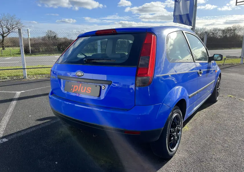 Vue 3/4 arrière droite d'une Ford Fiesta 1.3l essence 3 portes bleu vif avec jantes noires sur parking extérieur.