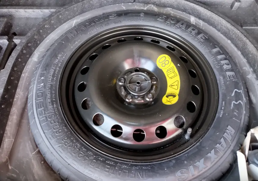 Gros plan sur la roue de secours noire du Ford Kuga gris clair, avec étiquette jaune indiquant la vitesse maximale 80 km/h.