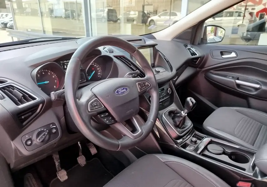 Intérieur du Ford Kuga 2019 vu côté conducteur, volant cuir, tableau de bord avec écran central et boîte manuelle.