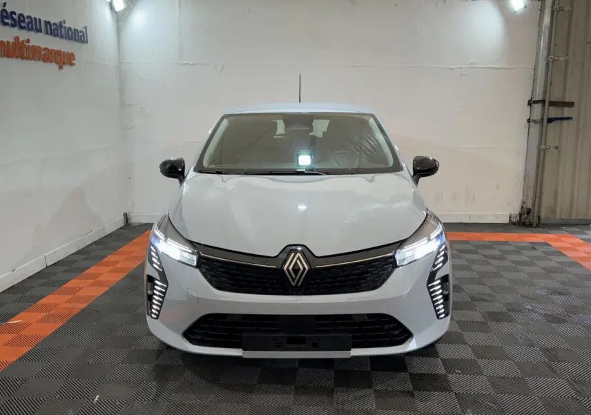 Vue avant d'une Renault Clio gris clair 2025 avec feux LED allumés et calandre noire dans un garage.