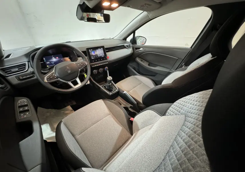 Intérieur de Renault Clio Evolution Blue dCi 100 2025, vue côté conducteur, sièges gris clair et tableau de bord moderne.