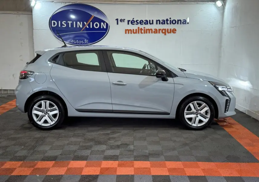 Profil côté gauche d'une Renault Clio gris clair 2025 dans un showroom avec logo Distinxion en arrière-plan.