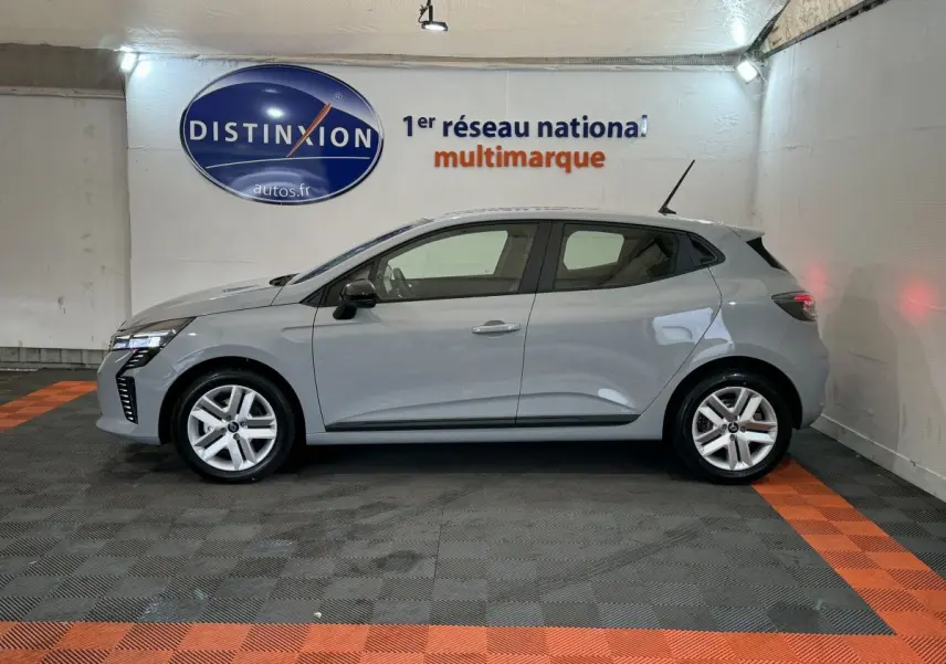 Profil côté gauche d'une Renault Clio gris clair 2025 dans un showroom avec éclairage intérieur et logo Distinxion en arrière-plan