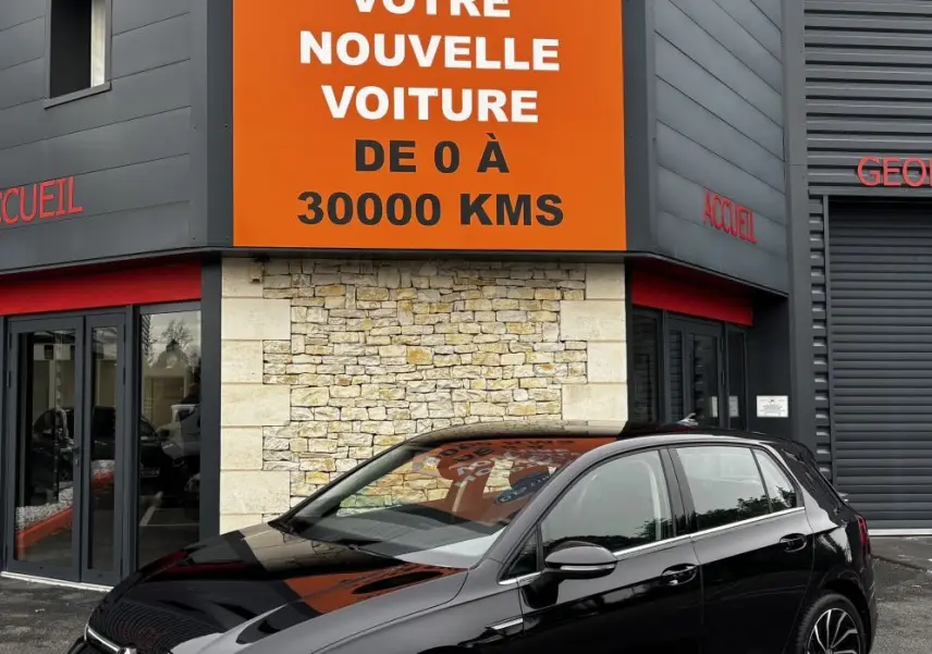 Volkswagen Golf noire vue en 3/4 avant droit, stationnée devant un bâtiment avec panneau orange Distinxion.