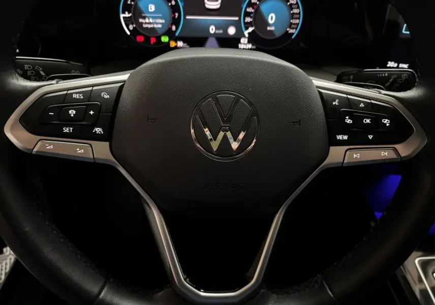 Vue rapprochée du volant cuir multifonctions d'une Volkswagen Golf 1.5 ETSI noire, avec tableau de bord digital lumineux.