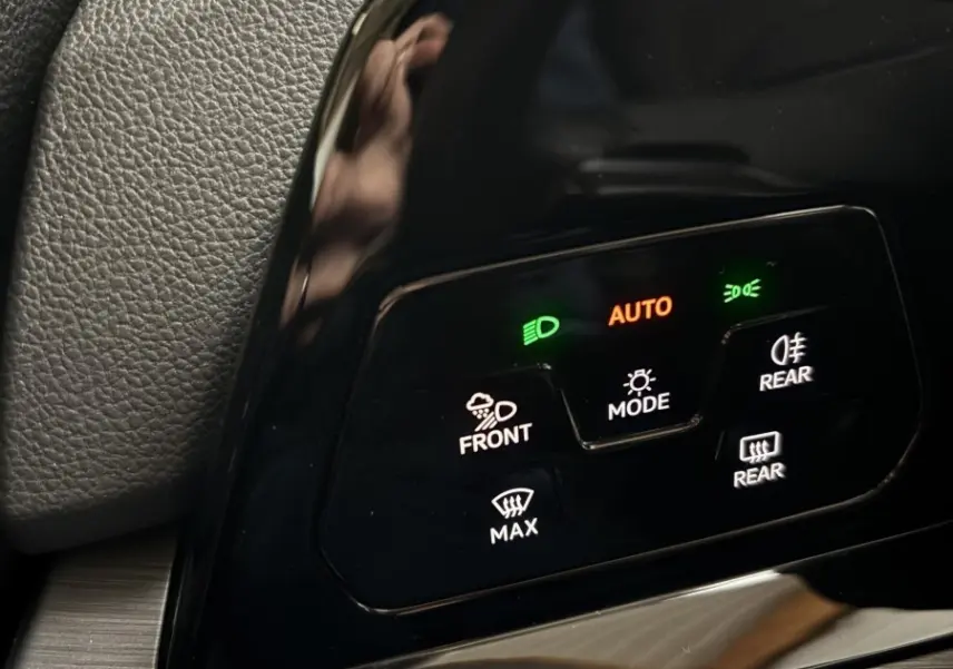 Gros plan sur le panneau de commandes d'éclairage noir brillant du Volkswagen Golf 2024, avec voyants verts et orange allumés.