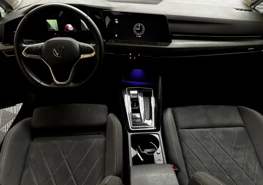 Vue intérieure avant de la Volkswagen Golf noire 2024, volant cuir, écran tactile et console centrale moderne éclairée.
