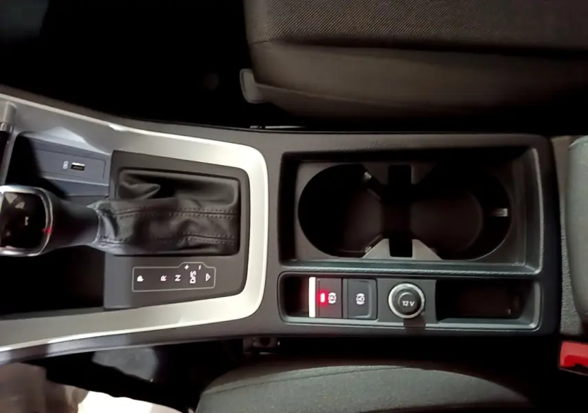 Vue plongeante sur la console centrale de l'Audi Q3 noir, avec levier de vitesse automatique et prises 12V visibles.