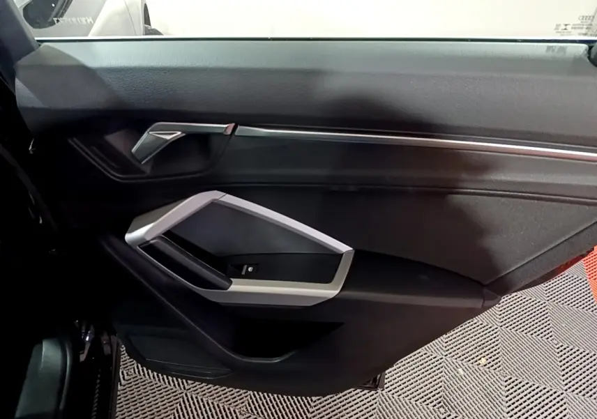 Vue intérieure du panneau de porte côté gauche noir de l'Audi Q3 35 TDI 150 S tronic Business Line avec poignée argentée.