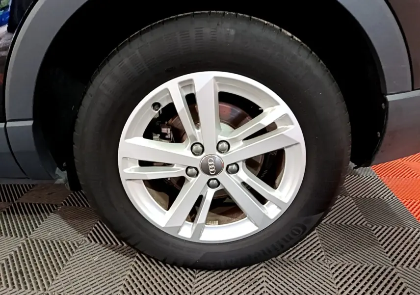 Gros plan sur la roue avant gauche avec jante argentée et logo Audi du SUV noir Audi Q3 35 TDI 2020.