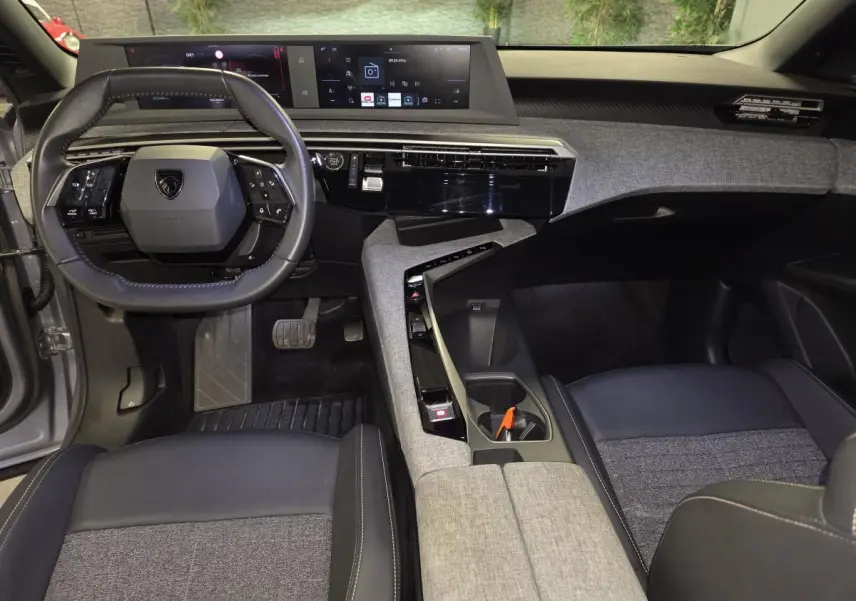 Vue intérieure du tableau de bord et volant Peugeot 3008 2025, avec sellerie tissu gris et console centrale design épuré.